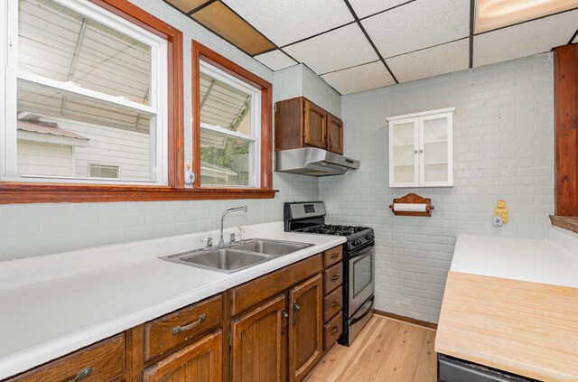 211 S Birney St, Bay City, MI 48708 - kitchen featuring stainless steel range with gas cooktop, a sink, under cabinet range hood, light wood-style floors, and a drop ceiling
