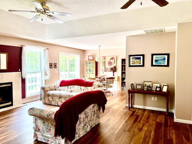 1745 Mullett Lake Woods Rd, Cheboygan, MI 49721 - living area featuring a ceiling fan, a textured ceiling, wood-type flooring, a tiled fireplace, and baseboards