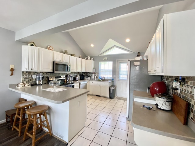 2476 W Branch Dr, West Branch, MI 48661 - kitchen featuring appliances with stainless steel finishes, a peninsula, backsplash, white cabinetry, and lofted ceiling