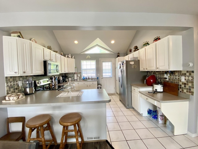 2476 W Branch Dr, West Branch, MI 48661 - kitchen featuring appliances with stainless steel finishes, a peninsula, decorative backsplash, lofted ceiling, and a breakfast bar area