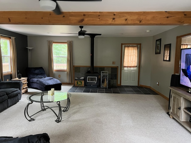 7781 N M-18, Roscommon, MI 48653 - carpeted living area featuring a wood stove, beam ceiling, ceiling fan, tile patterned floors, and baseboards