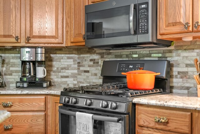 211 Gardners Grv, Roscommon, MI 48653 - kitchen featuring gas stove, decorative backsplash, light stone counters, and brown cabinetry
