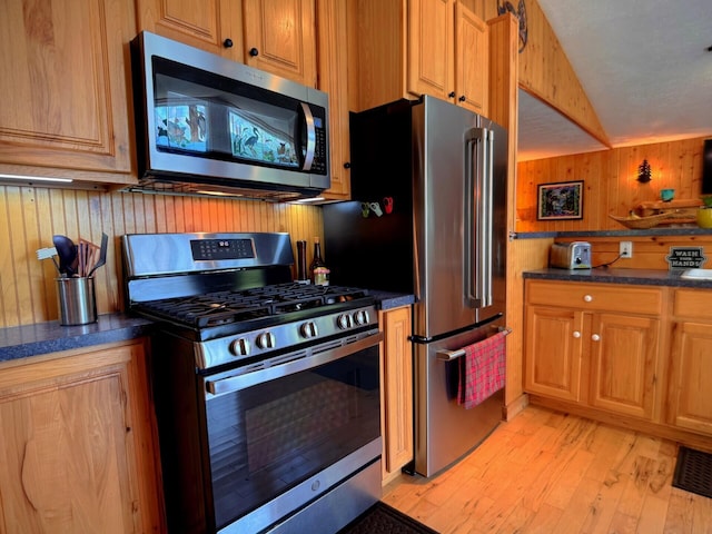 6309 Hiawatha Dr, Frederic, MI 49733 - kitchen with stainless steel appliances, wood walls, light wood-type flooring, vaulted ceiling, and brown cabinets
