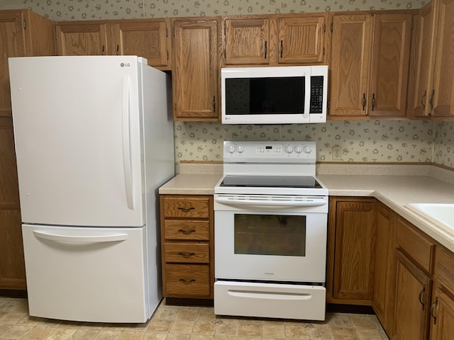 14501 3rd St, Hubbard Lake, MI 49747 - kitchen featuring white appliances, brown cabinetry, wallpapered walls, and light countertops