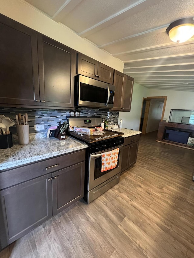 118 Westview Dr, Houghton Lake, MI 48629 - kitchen with stainless steel appliances, backsplash, light wood-style floors, dark brown cabinetry, and light stone countertops