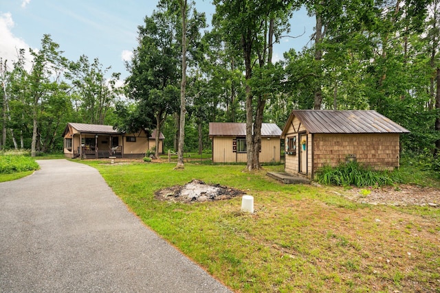 3065 E Dixon Lake Rd, Gaylord, MI 49735 - view of grassy yard featuring a porch, an outdoor structure, driveway, and view of wooded area