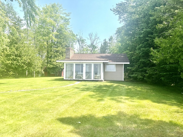 7811 Mcdonald Rd, Cheboygan, MI 49721 - rear view of property featuring a sunroom, a chimney, a yard, and a shingled roof