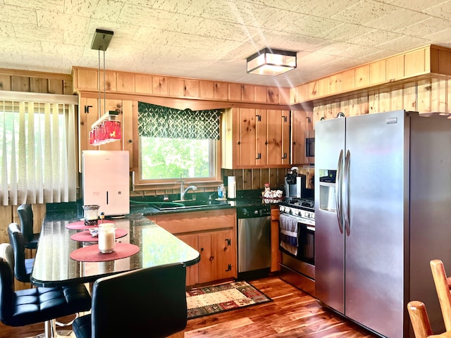 7811 Mcdonald Rd, Cheboygan, MI 49721 - kitchen featuring stainless steel appliances, wood finished floors, dark countertops, wood walls, and brown cabinetry