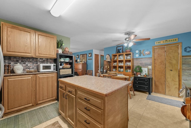 104 Alpena Trl, Houghton Lake, MI 48629 - kitchen with white microwave, ceiling fan, a kitchen island, light tile patterned floors, and decorative backsplash