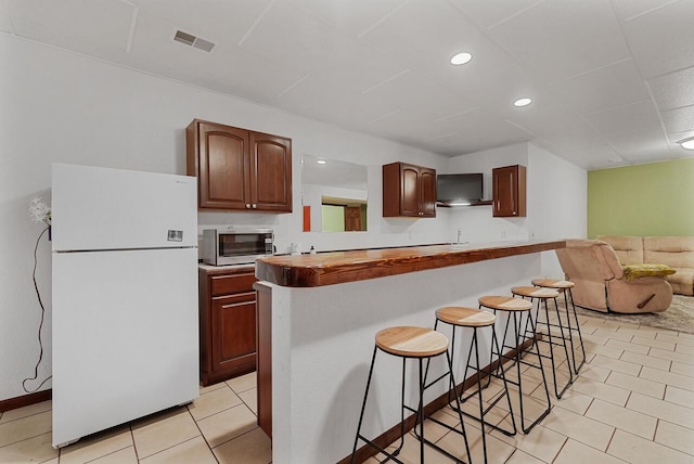 142 Frisco Dr, Houghton Lake, MI 48629 - kitchen with freestanding refrigerator, a breakfast bar, wall chimney range hood, open floor plan, and light tile patterned floors