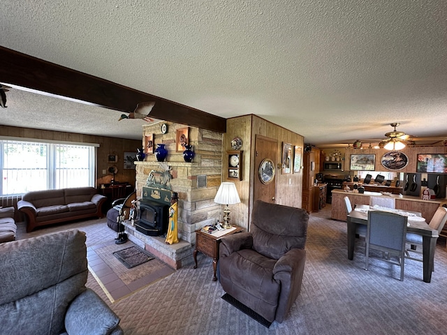 2585 M-33, Comins, MI 48619 - living room featuring a textured ceiling, wood walls, ceiling fan, carpet floors, and a wood stove