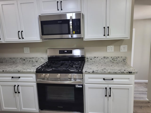 1251 Kingston Ave, Flint, MI 48507 - kitchen with stainless steel appliances, wood finished floors, white cabinets, and light stone countertops