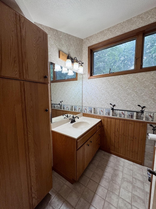 5200 Pine Grove Dr, Spruce, MI 48762 - bathroom with wallpapered walls, a textured ceiling, vanity, plenty of natural light, and a wainscoted wall