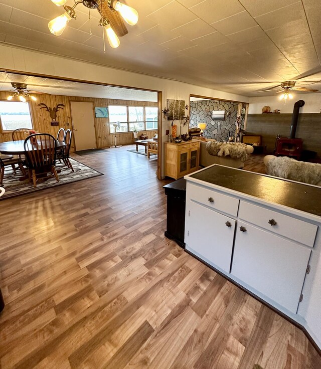 14781 Shubert Hwy, Posen, MI 49776 - kitchen with a ceiling fan, a wood stove, light wood-type flooring, and white cabinets