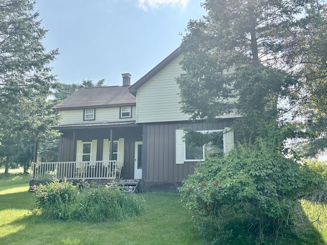 7770 Klein Rd, Hillman, MI 49746 - view of front facade with covered porch, a front lawn, board and batten siding, and a chimney