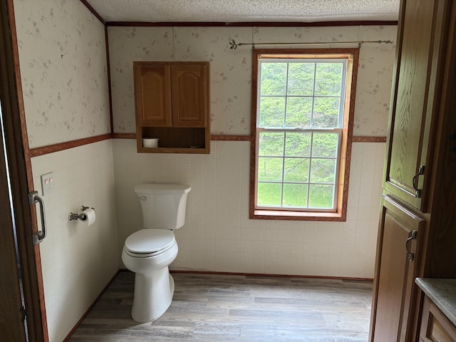 348 Lake Winyah Rd, Alpena, MI 49707 - bathroom featuring wood finished floors, wallpapered walls, a wainscoted wall, a textured ceiling, and tile walls