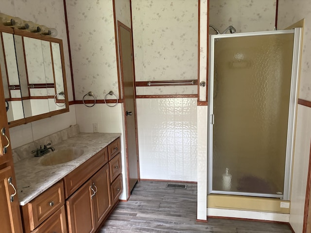 348 Lake Winyah Rd, Alpena, MI 49707 - bathroom featuring wallpapered walls, wood finished floors, vanity, a stall shower, and a wainscoted wall