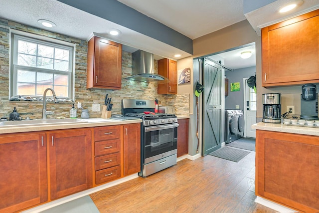 5514 N Bay Ct, Presque Isle, MI 49777 - kitchen featuring stainless steel gas stove, wall chimney exhaust hood, washer and dryer, a barn door, and light countertops