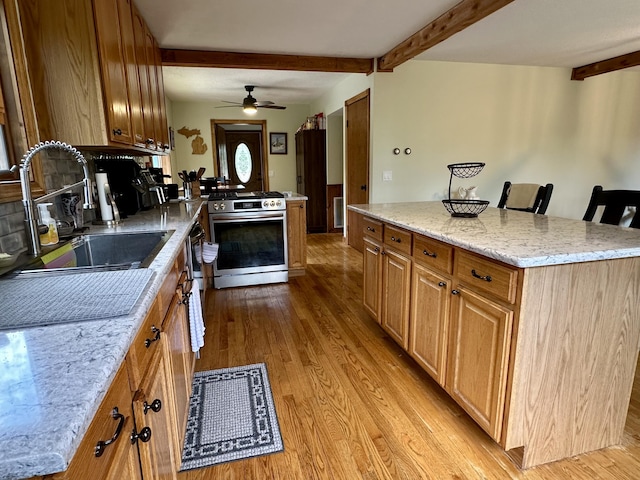 7984 US-23, Cheboygan, MI 49721 - kitchen with stainless steel range with gas stovetop, beamed ceiling, wood finished floors, a ceiling fan, and light stone countertops