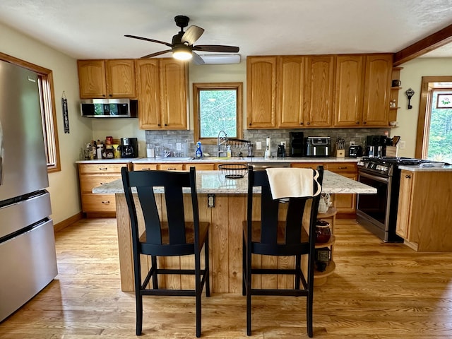 7984 US-23, Cheboygan, MI 49721 - kitchen featuring stainless steel appliances, backsplash, ceiling fan, light wood-style floors, and a breakfast bar