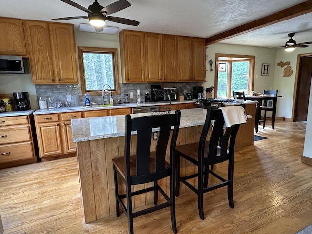 7984 US-23, Cheboygan, MI 49721 - kitchen featuring a ceiling fan, stainless steel microwave, backsplash, light wood-type flooring, and beam ceiling