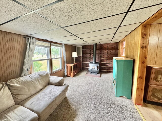 2833 S Horseshoe Trl, Grayling, MI 49738 - living area featuring a wood stove, wood walls, a paneled ceiling, and light colored carpet