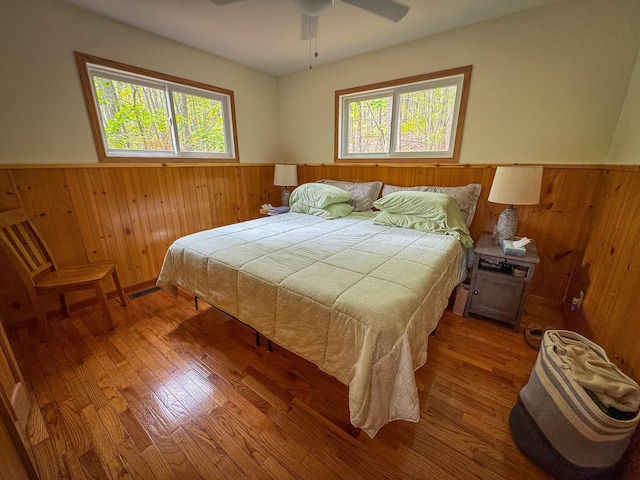 18680 Red Pine Dr, Hillman, MI 49746 - bedroom featuring wainscoting, wood walls, multiple windows, hardwood / wood-style flooring, and a ceiling fan