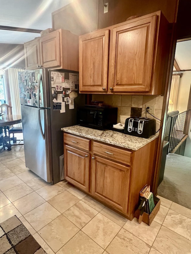 268 Yorke Trl, Grayling, MI 49738 - kitchen featuring black microwave, freestanding refrigerator, light stone counters, tasteful backsplash, and light tile patterned floors