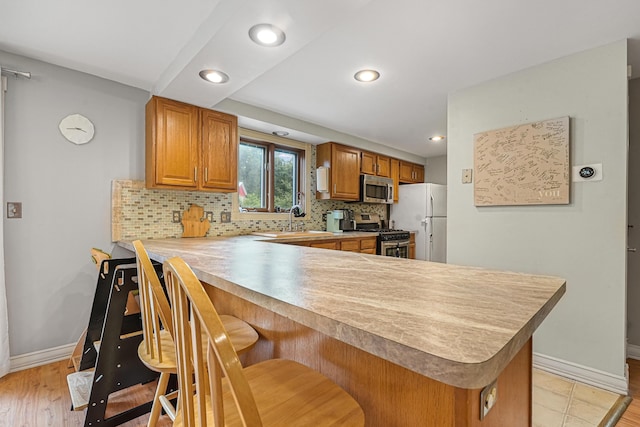 1655 Arrowhead Trl, West Branch, MI 48661 - kitchen featuring appliances with stainless steel finishes, brown cabinetry, decorative backsplash, light countertops, and a kitchen breakfast bar