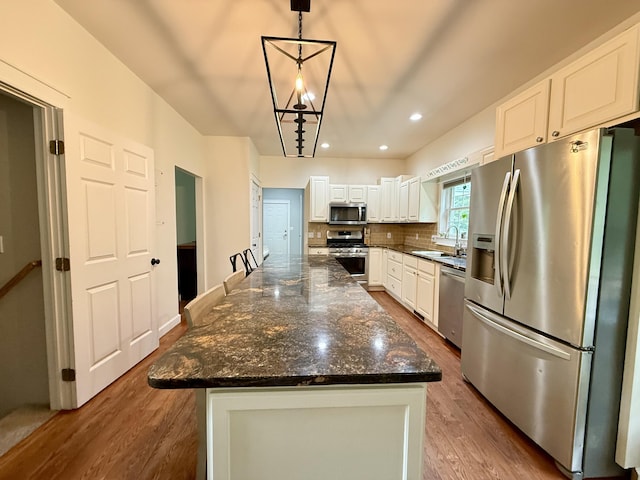 2176 Deepwoods Dr, Gaylord, MI 49735 - kitchen featuring stainless steel appliances, wood finished floors, white cabinets, a kitchen island, and tasteful backsplash