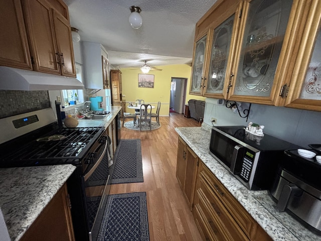 10604 Adams St, Ossineke, MI 49766 - kitchen with stainless steel appliances, under cabinet range hood, light wood finished floors, brown cabinetry, and glass insert cabinets