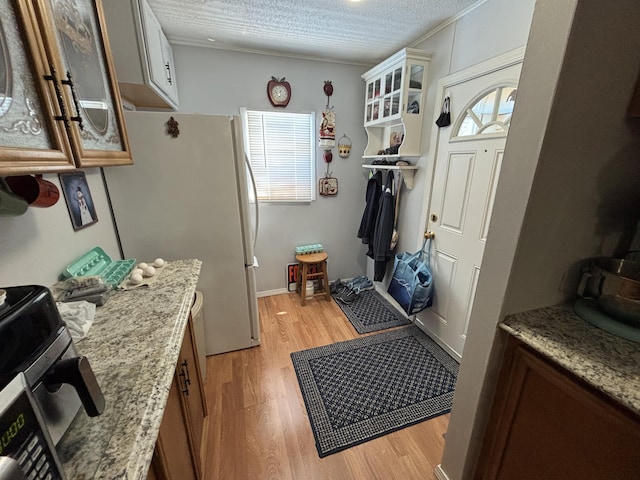 10604 Adams St, Ossineke, MI 49766 - kitchen with light wood-style floors, glass insert cabinets, freestanding refrigerator, light stone counters, and a textured ceiling