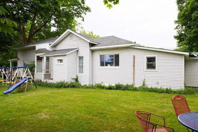 210 N Maple St, Mancelona, MI 49659 - rear view of property featuring a playground, roof with shingles, and a yard