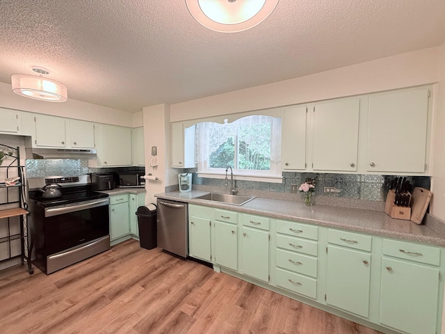 3628 Rau Rd, West Branch, MI 48661 - kitchen with appliances with stainless steel finishes, under cabinet range hood, a textured ceiling, light wood-style floors, and backsplash