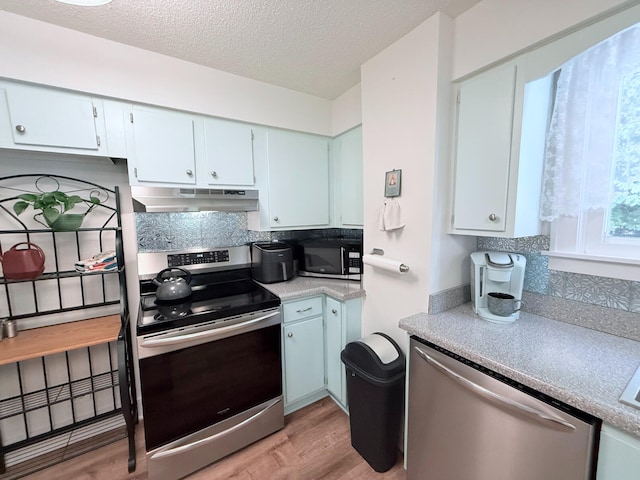 3628 Rau Rd, West Branch, MI 48661 - kitchen featuring stainless steel appliances, under cabinet range hood, backsplash, light wood finished floors, and a textured ceiling