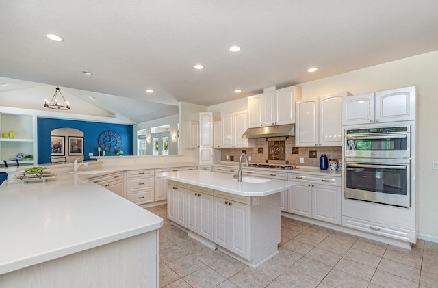 118 Frisco Dr, Houghton Lake, MI 48629 - kitchen with under cabinet range hood, stainless steel appliances, a center island with sink, lofted ceiling, and light countertops