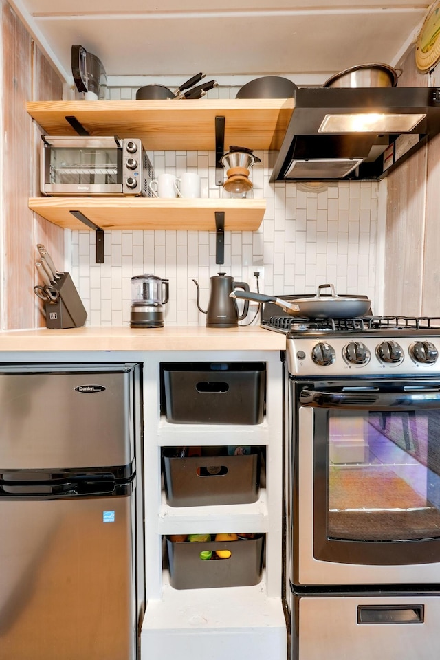 6390 W Houghton Lake Dr, Houghton Lake, MI 48629 - kitchen with stainless steel appliances, wall chimney exhaust hood, open shelves, decorative backsplash, and light countertops