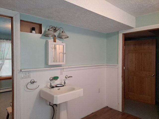 4160 S Vaughn Lake Rd, Glennie, MI 48737 - bathroom featuring a textured ceiling, wainscoting, wood finished floors, and a baseboard radiator