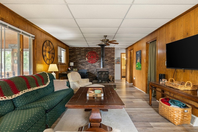 2731 Gregory St, Lewiston, MI 49756 - living room with wood walls, light wood-style flooring, a wood stove, a paneled ceiling, and a ceiling fan
