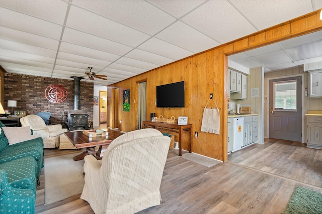 2731 Gregory St, Lewiston, MI 49756 - living room featuring a wood stove, a drop ceiling, wood walls, and light wood-style flooring