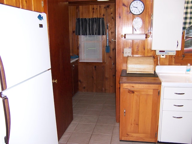 409 Marvin Rd, Roscommon, MI 48653 - kitchen featuring freestanding refrigerator, light tile patterned floors, wooden walls, and brown cabinets
