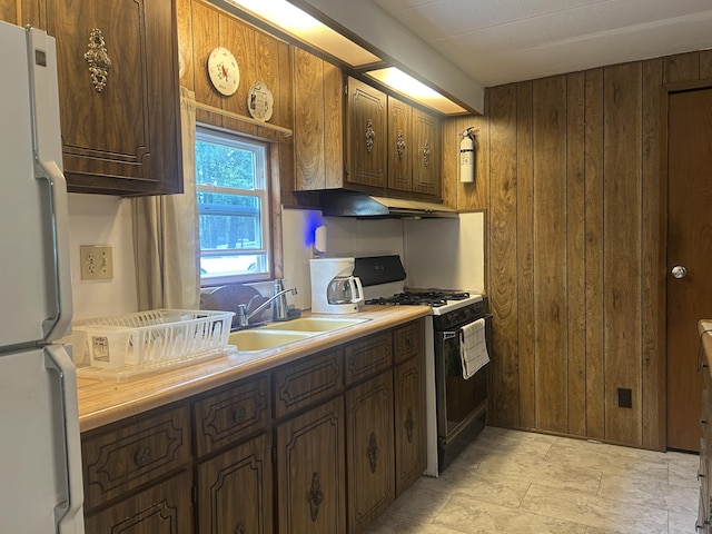 15939 Hiawatha Trl, Atlanta, MI 49709 - kitchen featuring gas stove, freestanding refrigerator, wooden walls, under cabinet range hood, and light countertops