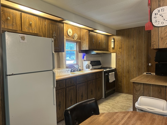 15939 Hiawatha Trl, Atlanta, MI 49709 - kitchen featuring freestanding refrigerator, black gas range oven, wooden walls, under cabinet range hood, and light countertops