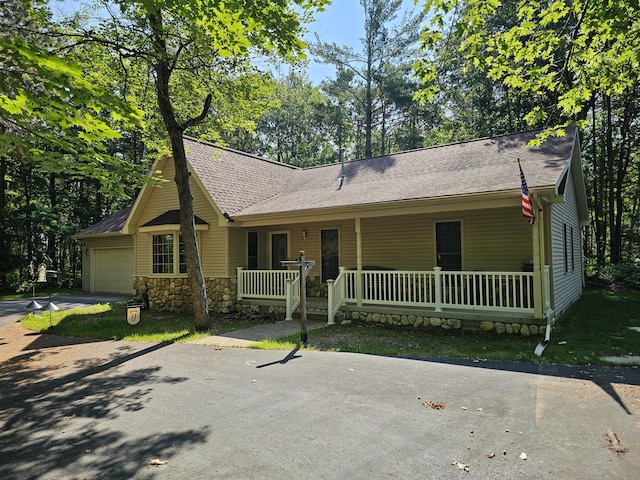 14911 Kings Ln, Ocqueoc, MI 49759 - view of front of house with a porch, driveway, a garage, stone siding, and a shingled roof