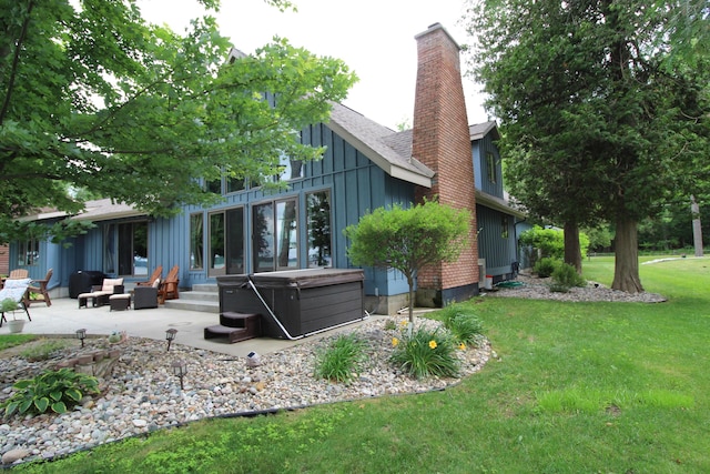 2150 Danish Landing Rd, Grayling, MI 49738 - back of property with board and batten siding, a patio area, a chimney, a yard, and a hot tub