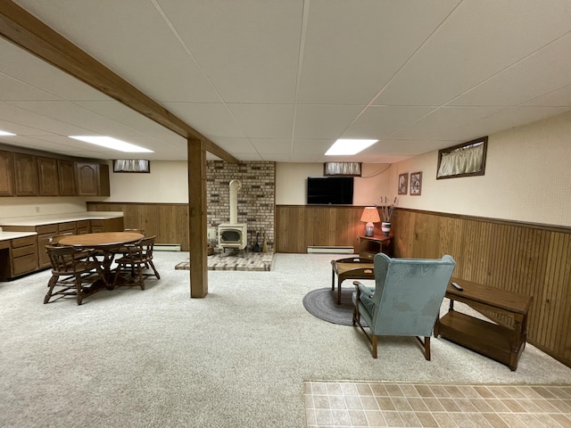 982 Shaggy Bark Ct, Gaylord, MI 49735 - living room featuring light colored carpet, a drop ceiling, a wood stove, a wainscoted wall, and a baseboard radiator