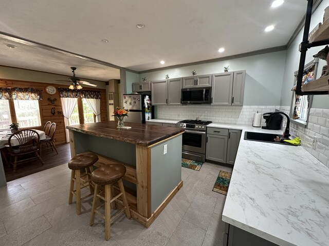 5127 Crestwood Rd, Lewiston, MI 49756 - kitchen featuring stainless steel appliances, gray cabinetry, crown molding, a center island, and a breakfast bar area