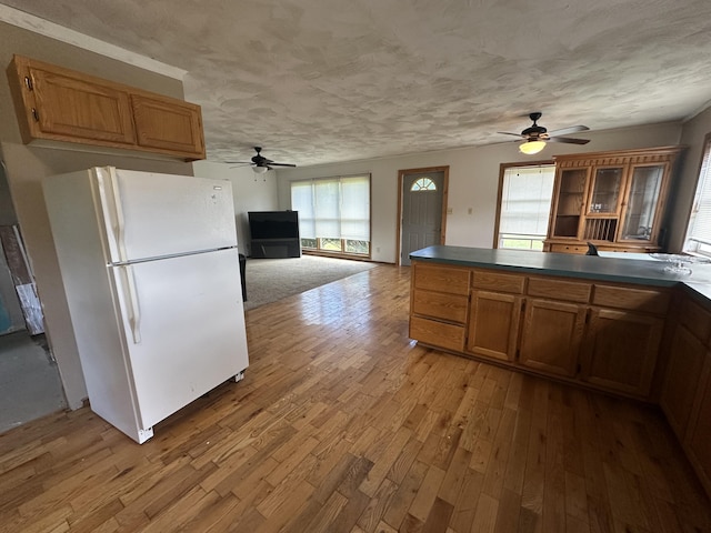 4974 Meridian Line Rd, Johannesburg, MI 49751 - kitchen featuring freestanding refrigerator, a ceiling fan, wood finished floors, brown cabinets, and a textured ceiling
