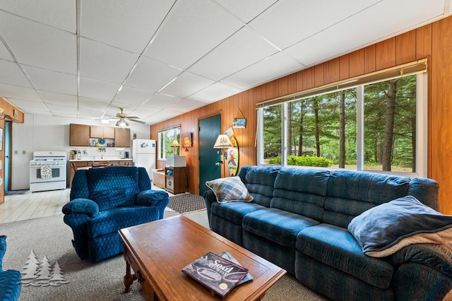 2911 Birch St, Lewiston, MI 49756 - living room featuring plenty of natural light, light colored carpet, a drop ceiling, wood walls, and ceiling fan