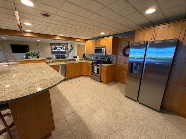 169 Pine Bluffs Rd, Roscommon, MI 48653 - kitchen with stainless steel appliances, a peninsula, light stone counters, tasteful backsplash, and brown cabinets